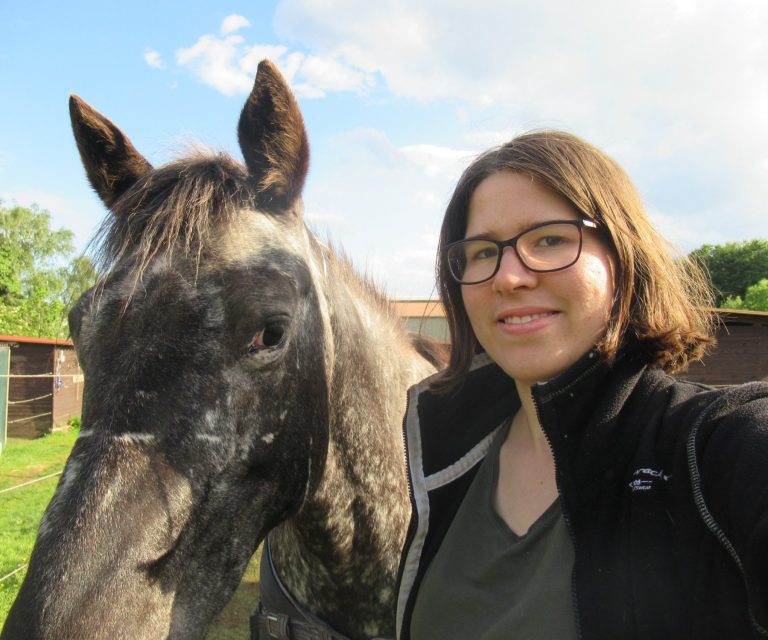 Coach Annika Mücke schaut zusammen mit Pferd in Kamera